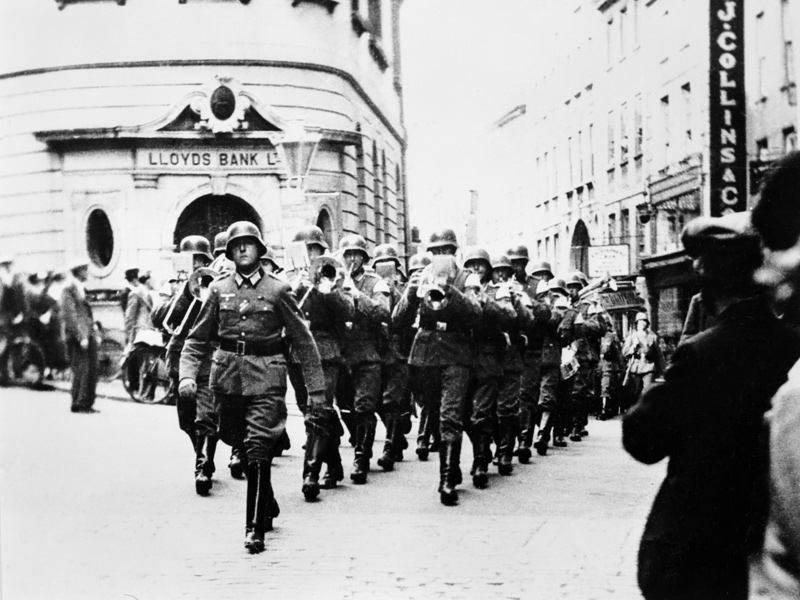 German military band marching past Lloyds Bank on The Pollet, St Peter Port. © IWM